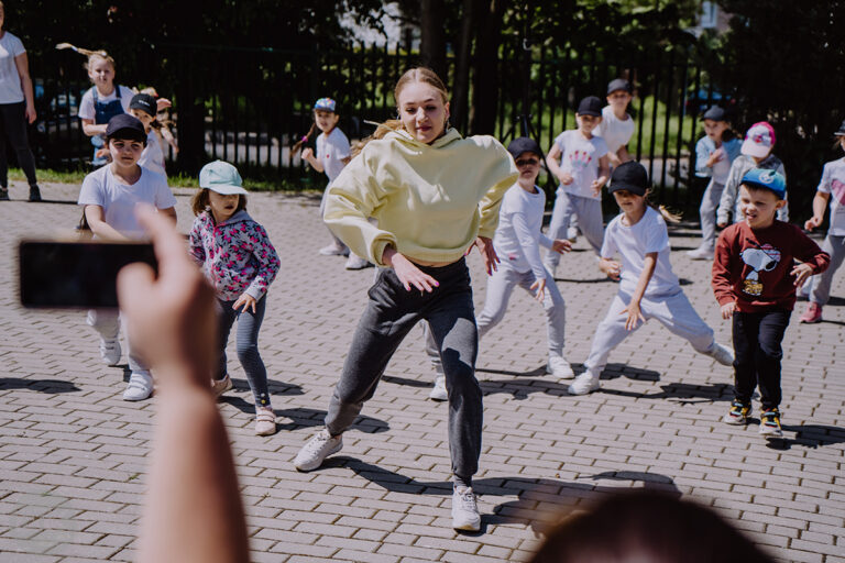 Młoda kobieta i grupa dzieci; wszyscy tańczą.